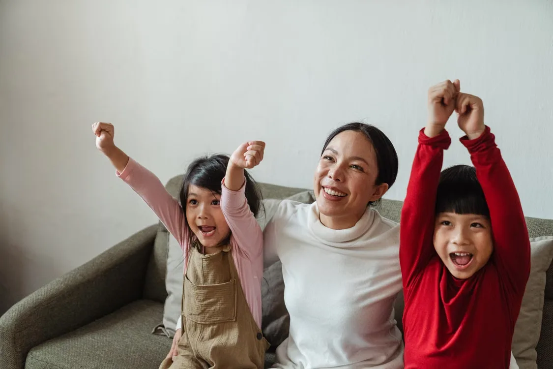 A mom and her two kids cheering together on the couch